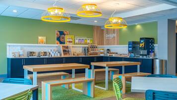 A modern café with wooden tables and benches, a counter with food items, and bright yellow pendant lights.