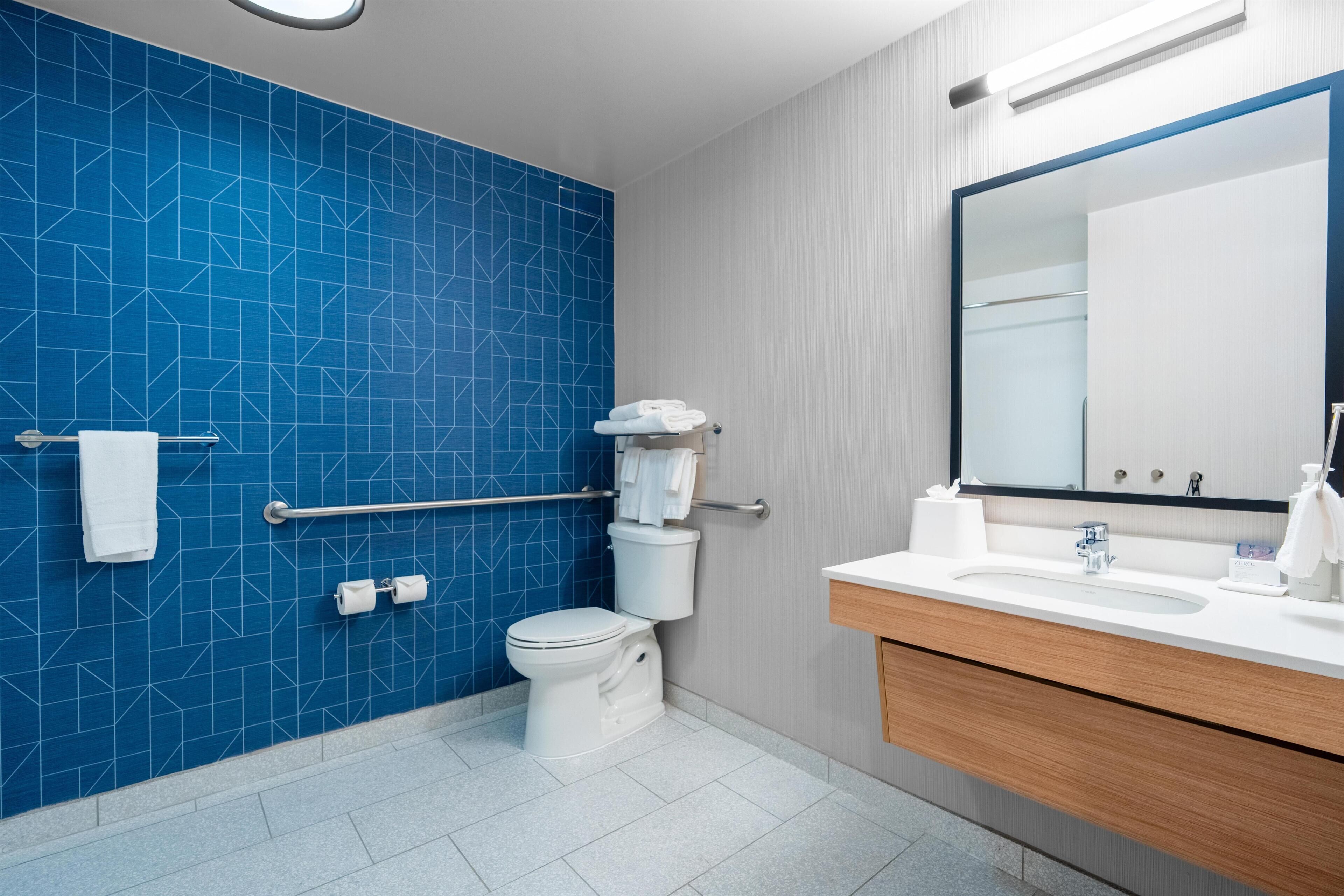 Een moderne badkamer met een blauwe betegelde muur, een wit toilet, een wastafel met spiegel en een houten wastafelmeubel.