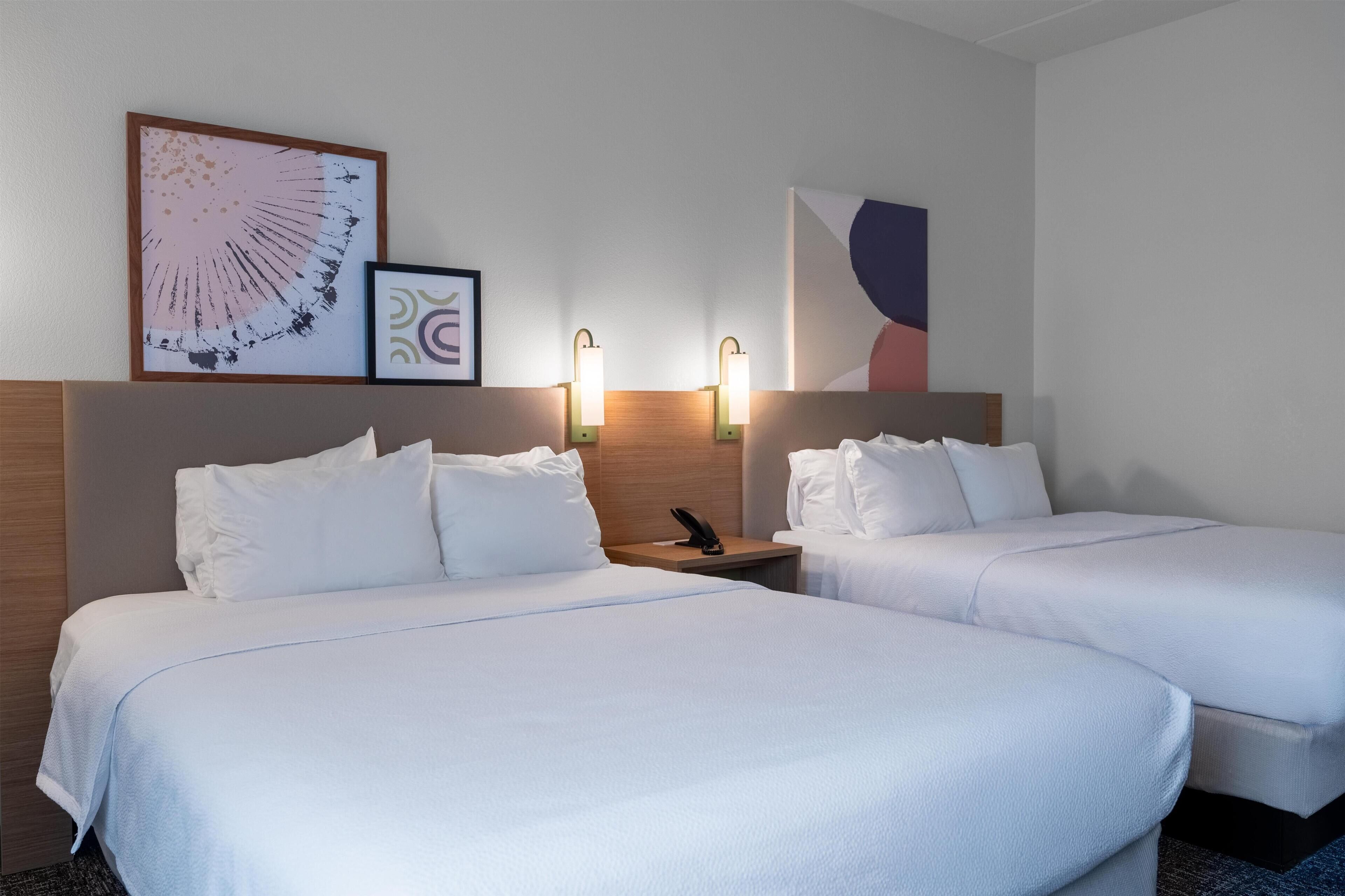 Een hotelkamer met twee bedden, een houten hoofdbord, wandlampen en ingelijste kunstwerken.