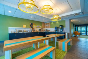 A modern café with wooden tables and benches, a kitchen area, and a seating area with a view. - Spark by Hilton Atlanta Kennesaw Town Center (Kennesaw)
