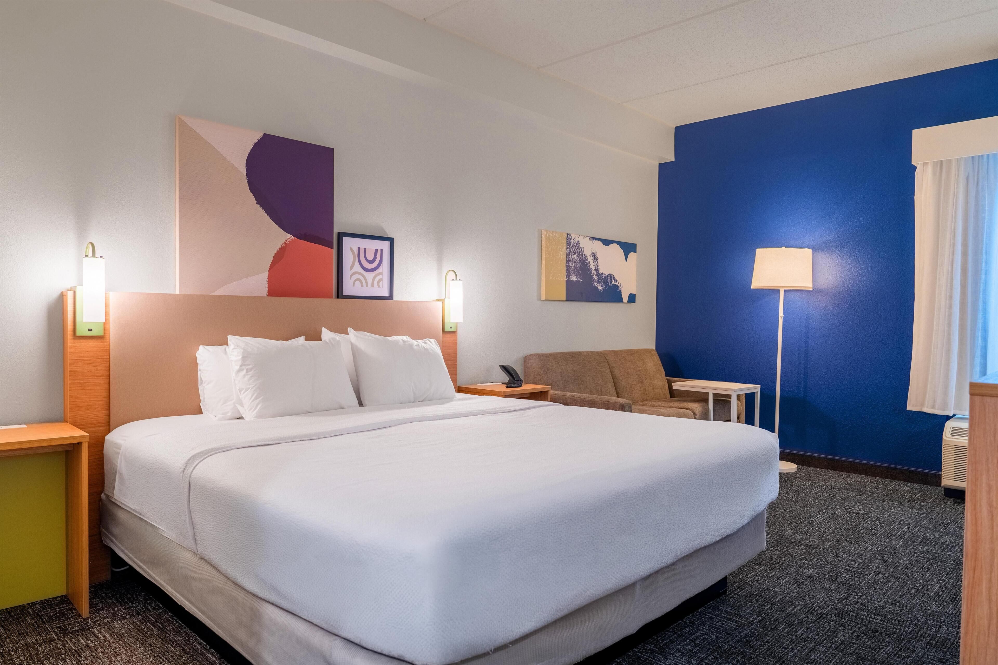 Une chambre d’hôtel avec un grand lit, des tables de chevet, un bureau, une chaise et des œuvres d’art accrochées aux murs.