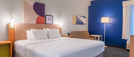 A hotel room with a large bed, bedside tables, a desk, a chair, and artwork on the walls.