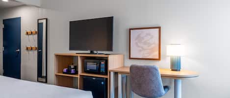 A hotel room with a bed, a desk with a chair, a television, a microwave, a refrigerator, and a framed picture on the wall.