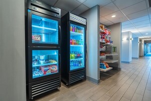 Um corredor com duas vitrines refrigeradas contendo bebidas e lanches, e uma estante com diversos itens.