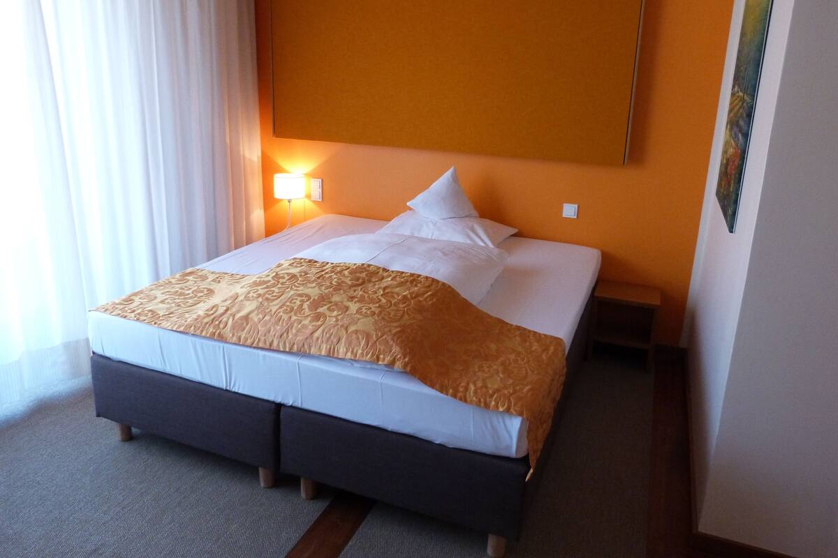 A hotel room with a bed, a nightstand, a lamp, and a painting on the wall.