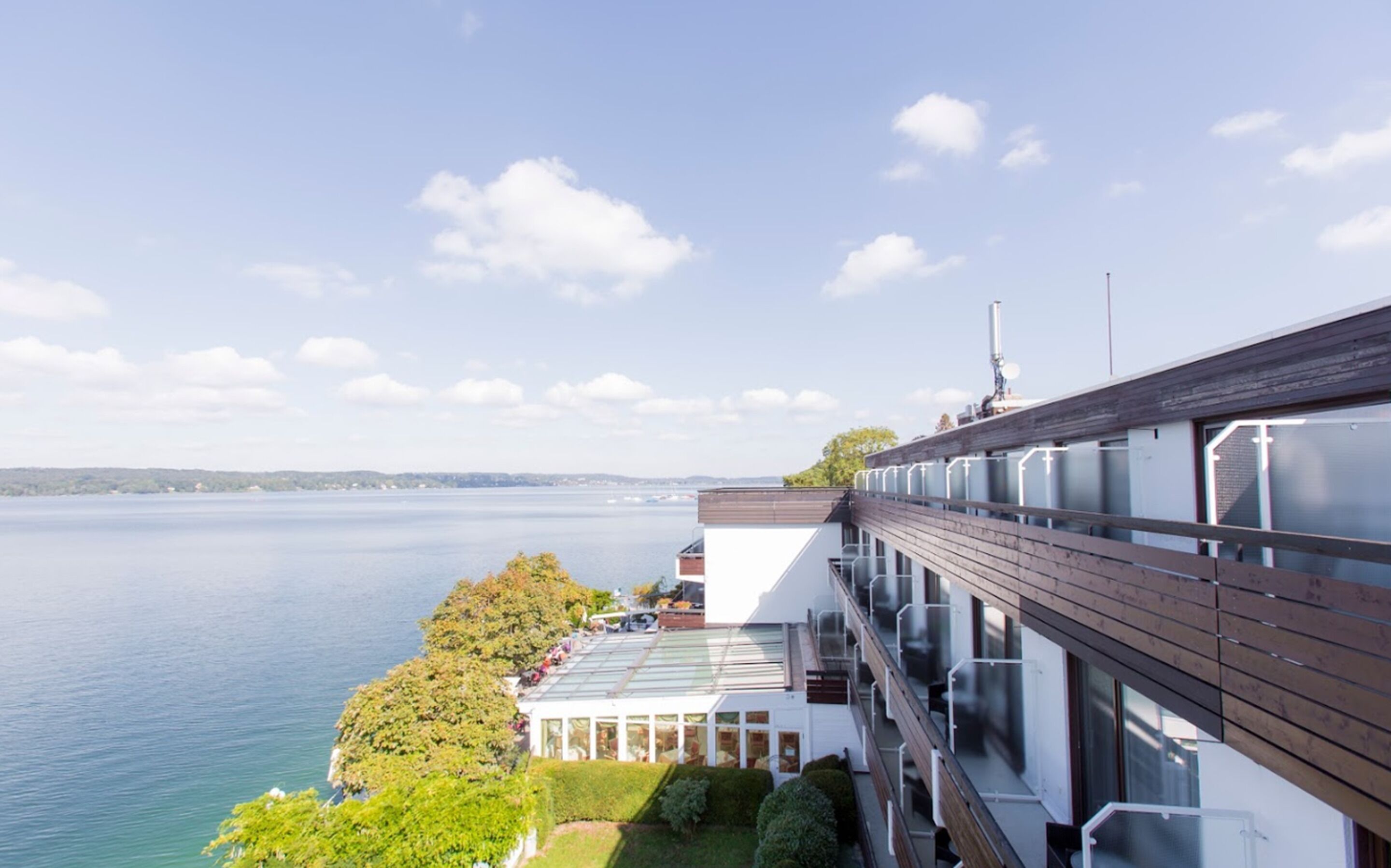 A modern building with a glass conservatory, a wooden deck, and a view of a lake.