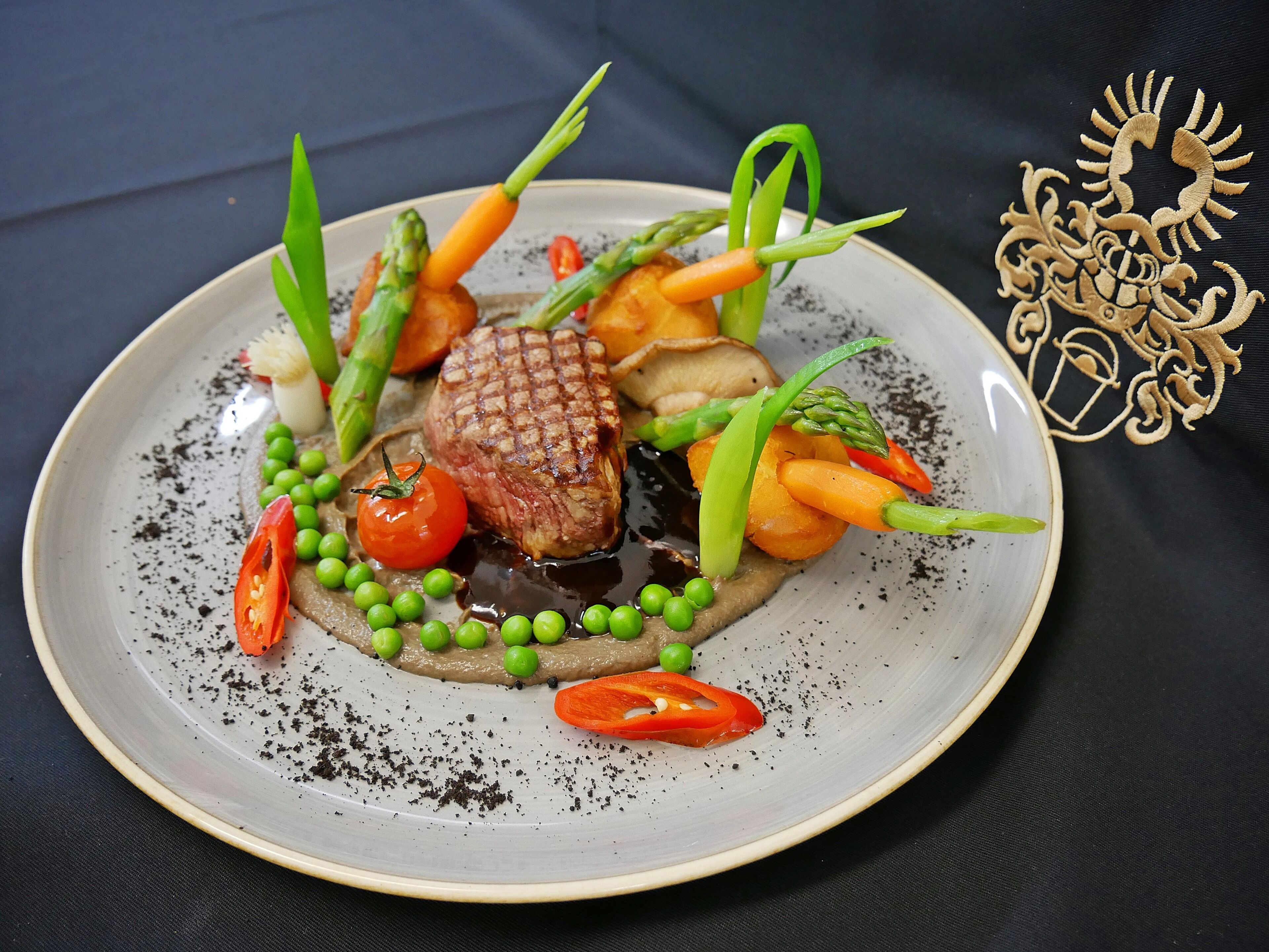 Ein Teller mit Essen, darunter ein Steak, Spargel, Karotten, Erbsen und Kirschtomaten.