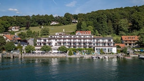 Un hotel con un edificio grande, barcos amarrados y una ladera boscosa al fondo.