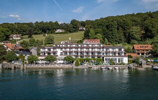 Um hotel com um edifício grande, barcos atracados e uma encosta arborizada ao fundo.