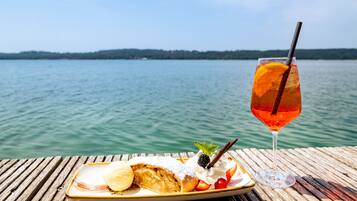 A wooden table with a dessert plate and a glass of drink by a lake.