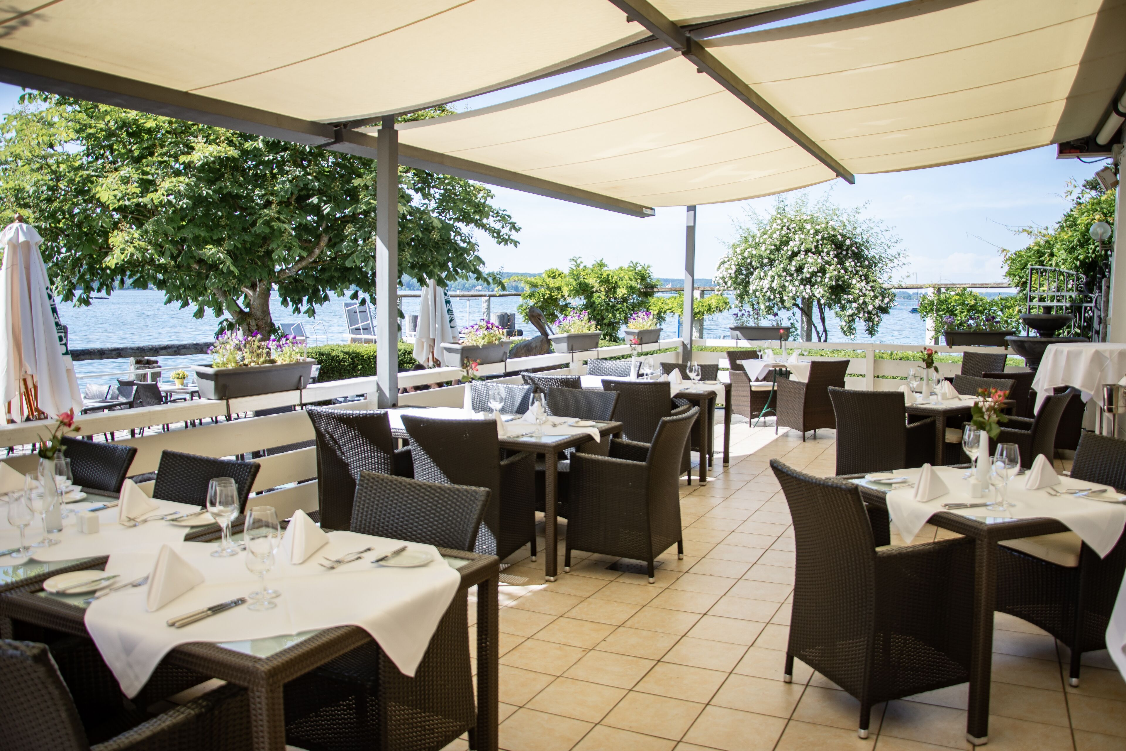 An outdoor dining area with tables and chairs, overlooking a body of water.
