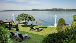Un espacio al aire libre junto al lago con sillones de descanso, sombrillas y un pabellón.