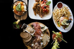 Diverse pietanze tra cui una ciotola di zuppa, un piatto di waffle, un piatto di patatine fritte, un tagliere di salumi e una bevanda con guarnizione da cocktail.