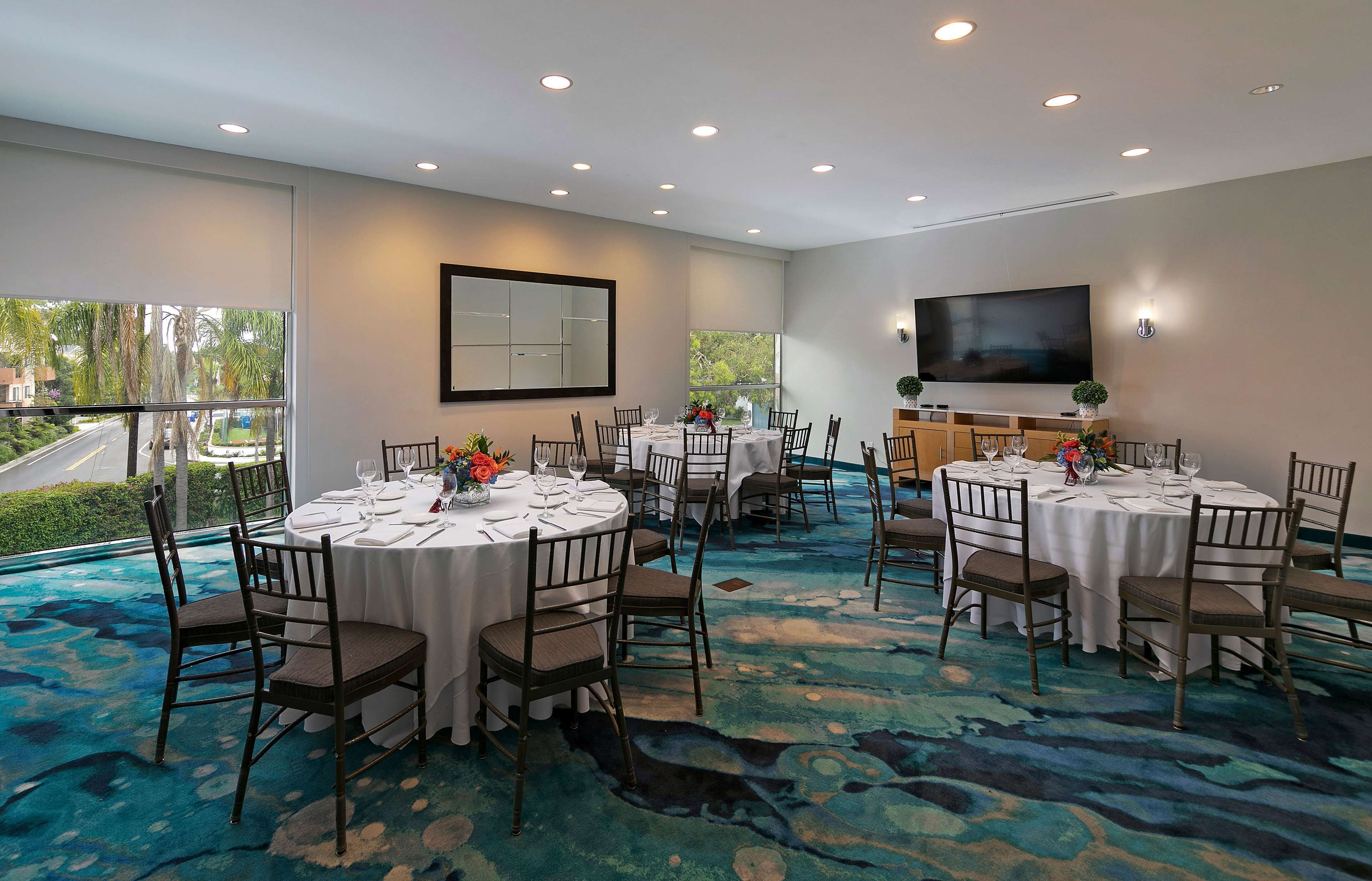 A conference room with round tables, chairs, a large TV, and a view of the outdoors.