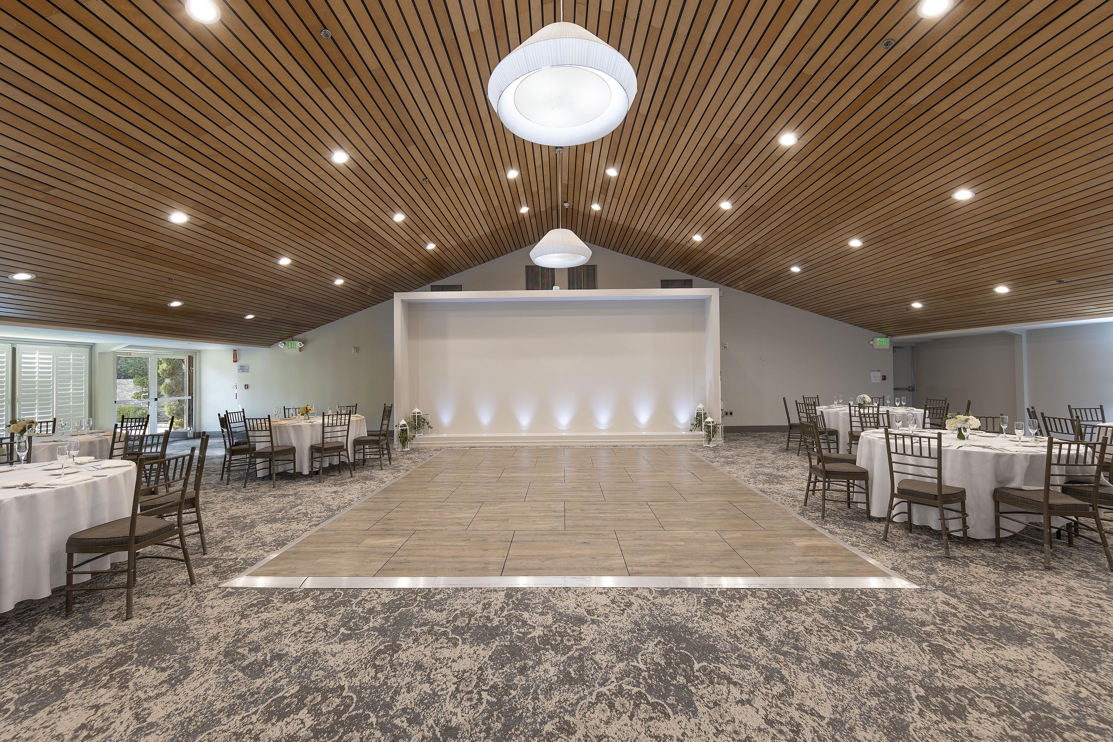 A spacious hall with a high wooden ceiling and recessed lighting, arranged for a formal event or conference.