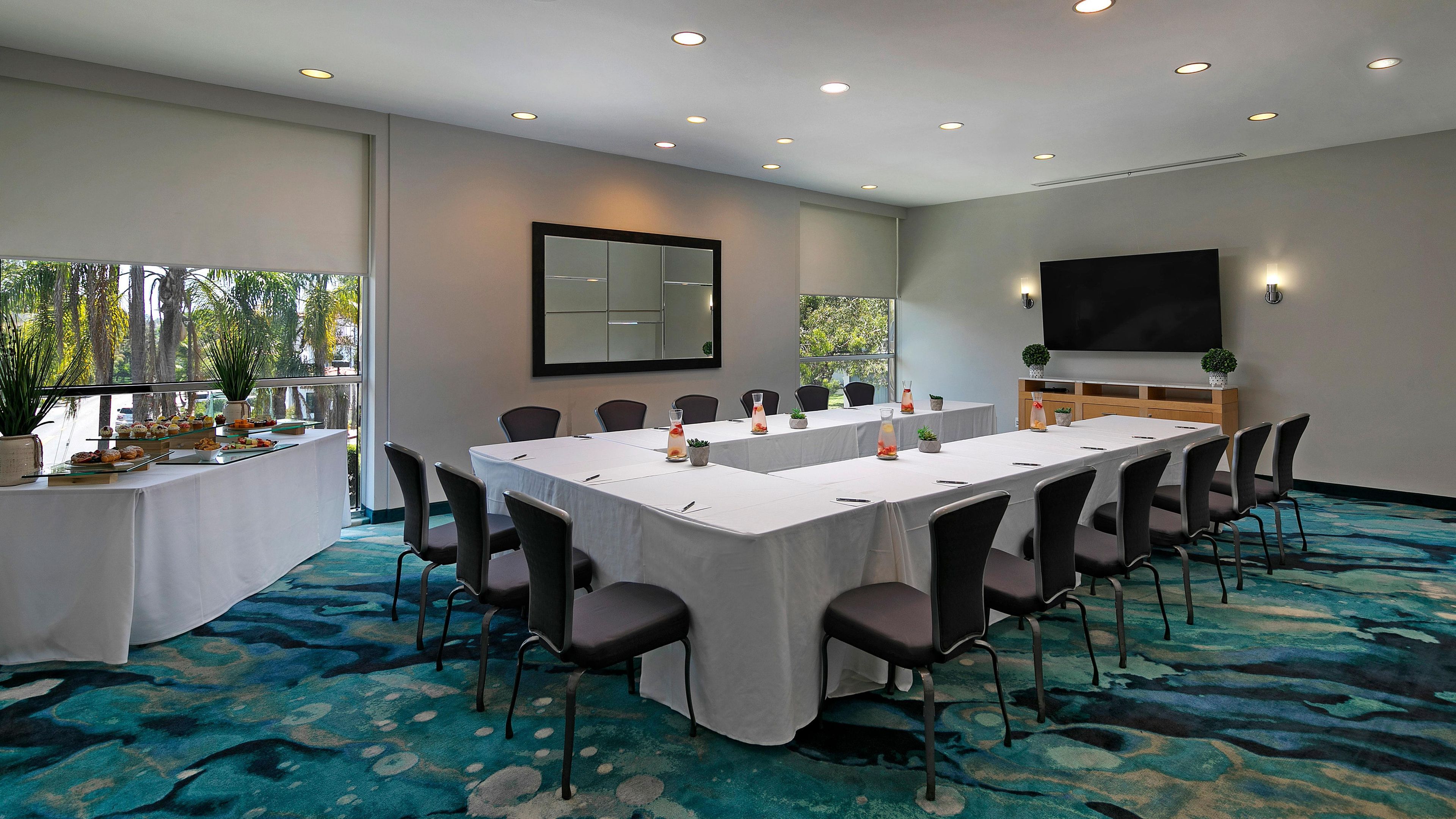 Un salón de conferencias con una larga mesa, sillas, una pantalla de televisión y una mesa de buffet con comida.