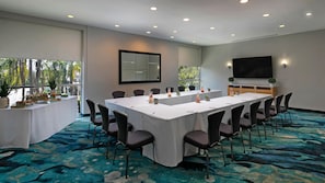 Une salle de conférence équipée d’une longue table, de chaises, d’un écran de télévision et d’une table de buffet où sont disposés des plats.