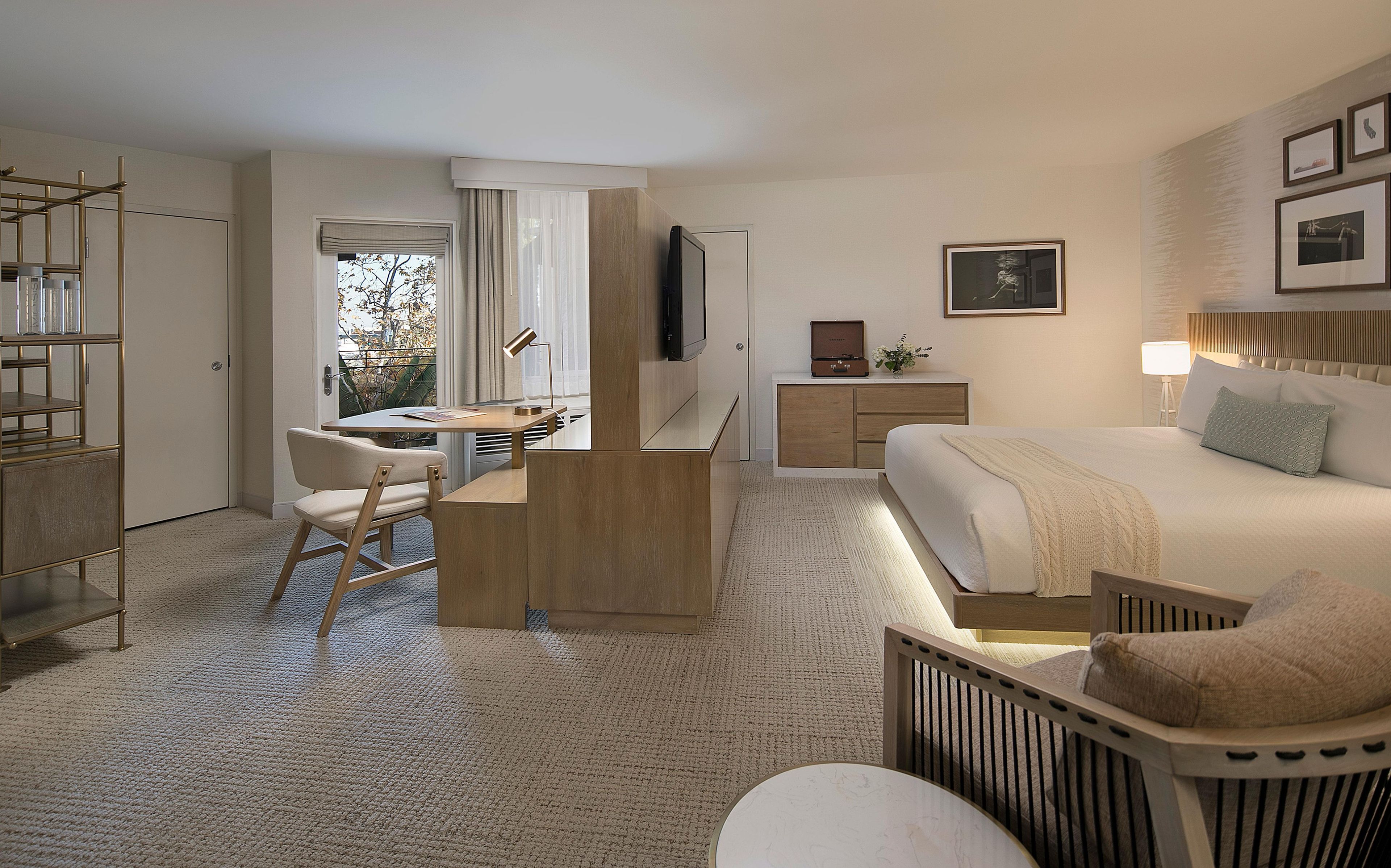 Habitación de hotel con cama, escritorio, silla, televisor, mesita de noche y ventana con cortinas.