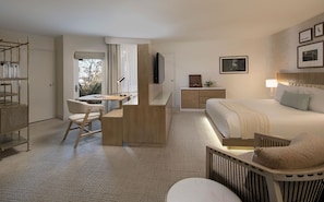 Une chambre d’hôtel comprenant un lit, un bureau, une chaise, une télévision, une table de chevet et une fenêtre avec des rideaux.