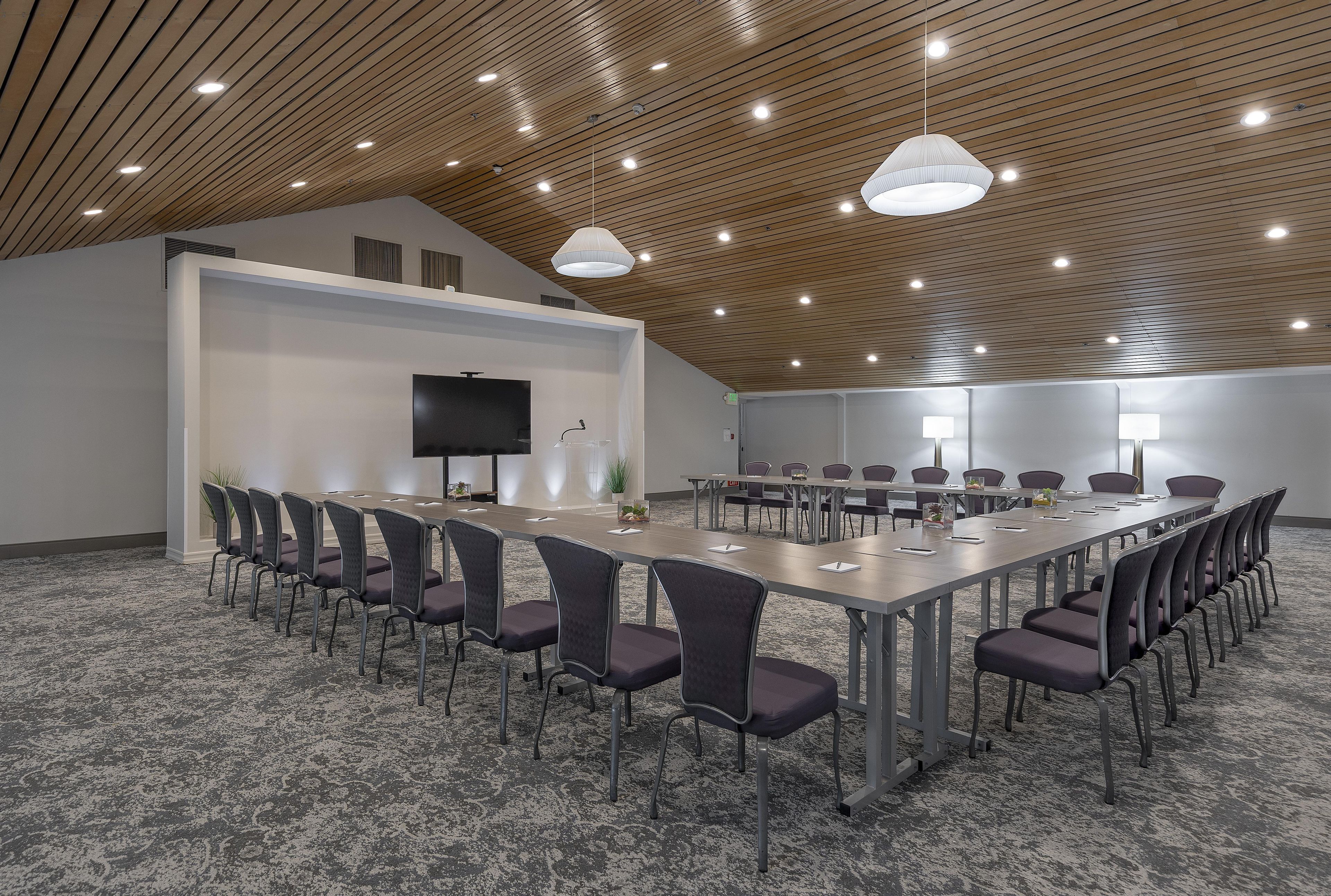A conference room with a long table, chairs, a flat-screen TV, and a ceiling with wooden slats and recessed lighting.