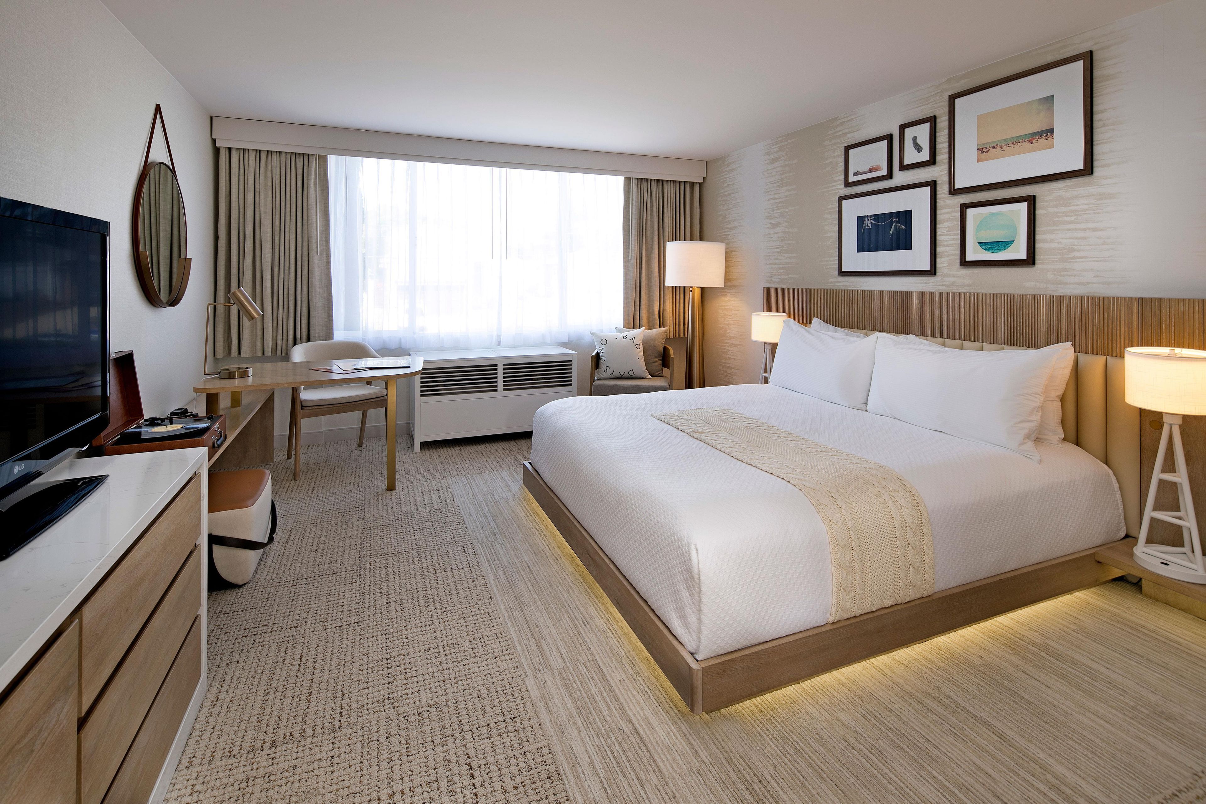 Habitación de hotel con cama, escritorio, silla, televisor y lámparas fijadas a la pared.