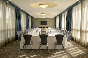Een vergaderzaal met een lange tafel, stoelen en een televisiescherm.