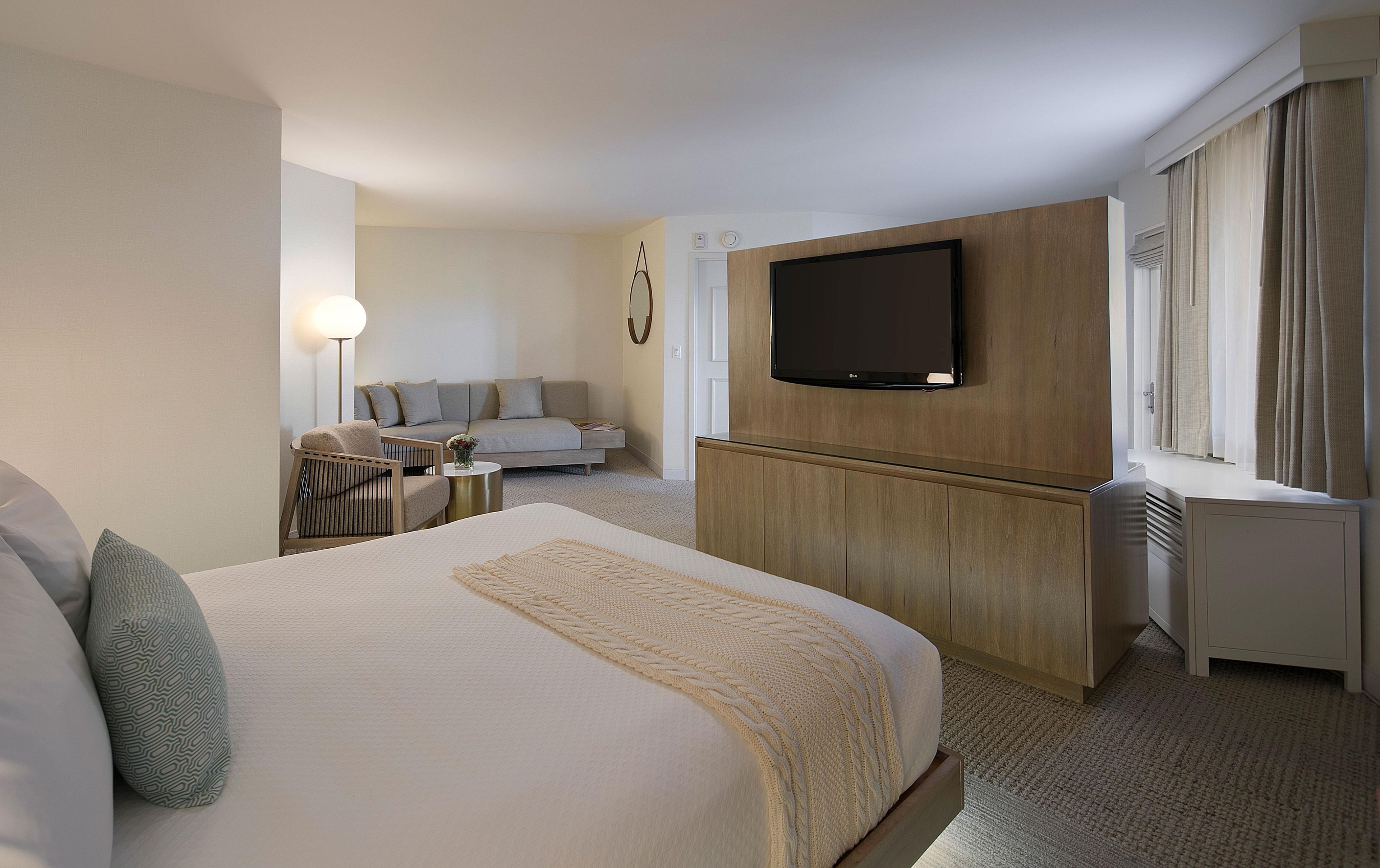 Ein Hotelzimmer mit einem großen Bett, einer Couch, einem an der Wand montierten Fernseher und einem Fenster mit Vorhängen.