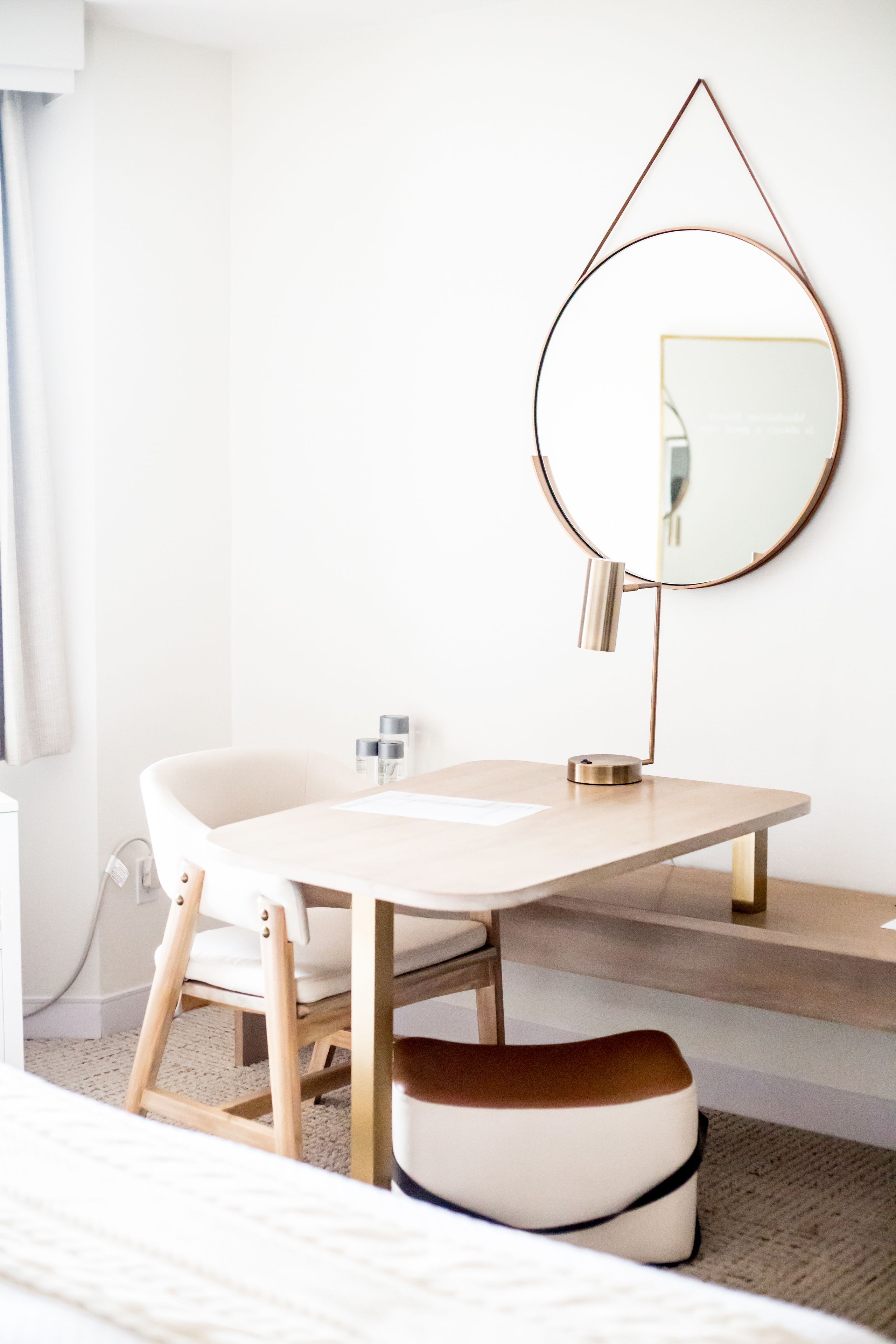Un baño moderno con un tocador blanco, un espejo redondo y una silla de madera.