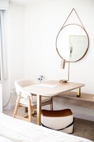 Un baño moderno con un tocador blanco, un espejo redondo y una silla de madera.