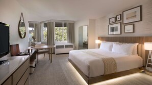 A hotel room with a large bed, a desk, a chair, a TV, and a window with curtains. - Belamar Hotel Manhattan Beach, Tapestry Collection by Hilton (Manhattan Beach)