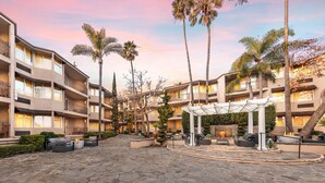 A courtyard with outdoor seating, palm trees, and a building with balconies. - Belamar Hotel Manhattan Beach, Tapestry Collection by Hilton (Manhattan Beach)