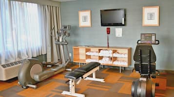 A gym with exercise equipment, a bench, a television, and framed pictures on the wall.