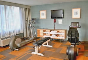 Un gimnasio con equipo de ejercicio, una banca, una televisión y cuadros en la pared.