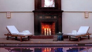 A poolside area with two lounge chairs, a fireplace with candles, and a framed picture above the fireplace. - Belamar Hotel Manhattan Beach, Tapestry Collection by Hilton (Manhattan Beach)