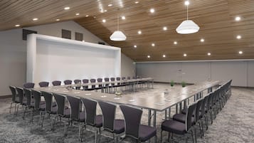A conference room with a long table, chairs, a projector screen, and ceiling lights.