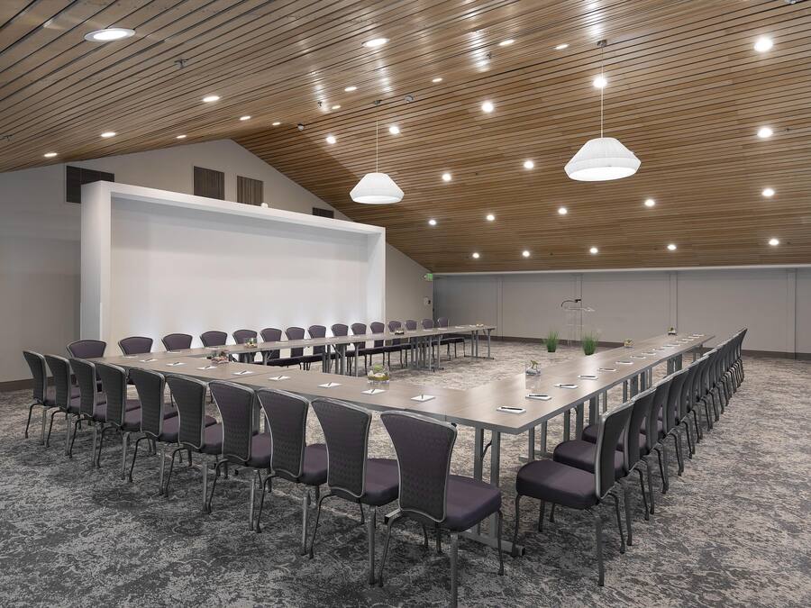 A conference room with a long table, chairs, a projector screen, and ceiling lights.
