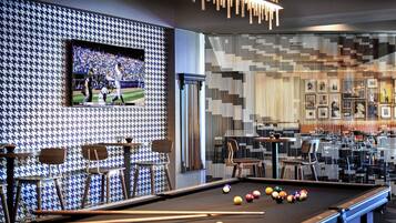 A billiards table with balls, a television displaying a sports event, and a patterned wall with framed pictures.