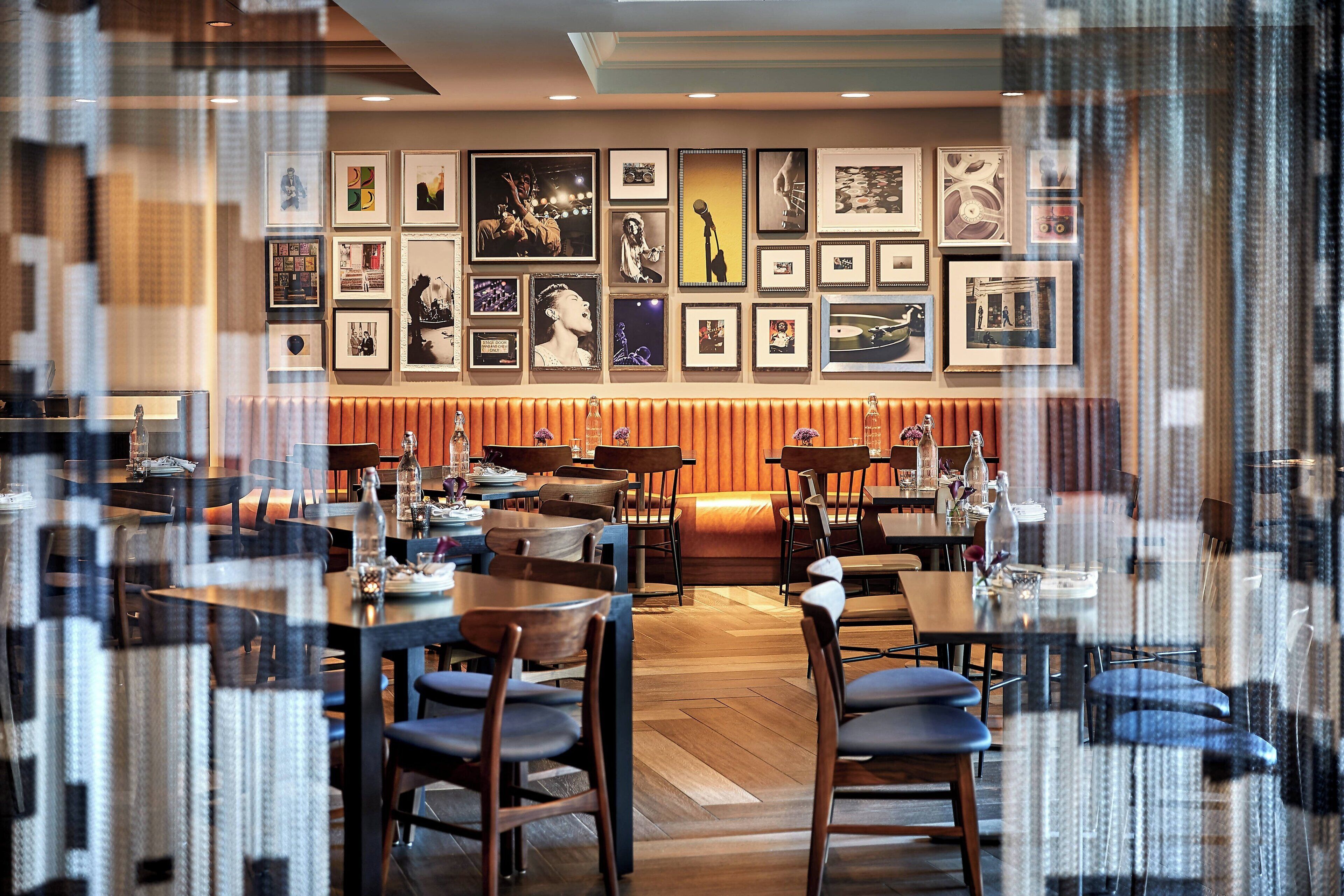 A restaurant with multiple tables and chairs, a wall decorated with framed pictures, and a wooden floor.