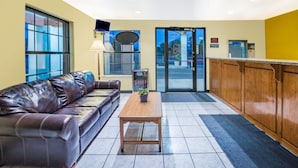 A reception area with a leather sofa, a wooden table, and a glass door leading outside. - Days Inn by Wyndham McAllen (McAllen)