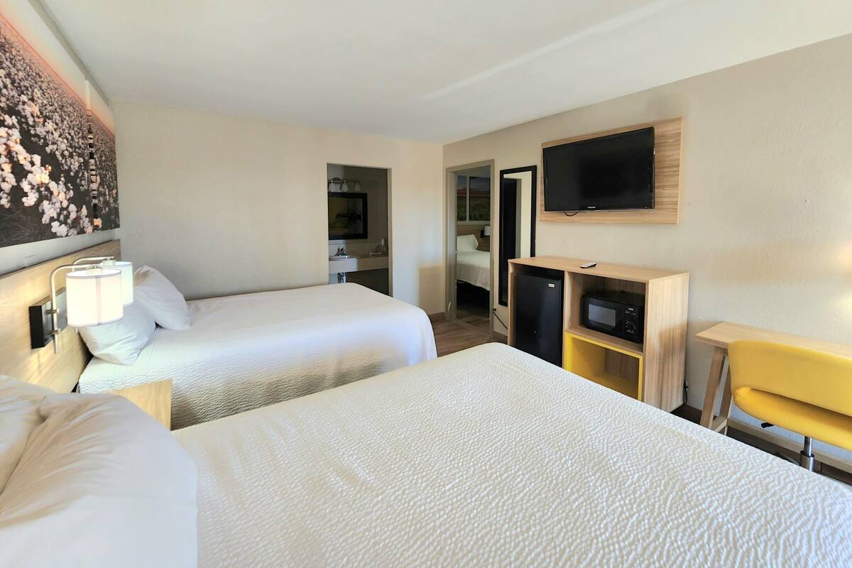A hotel room with two beds, a TV, a microwave, and a small desk.