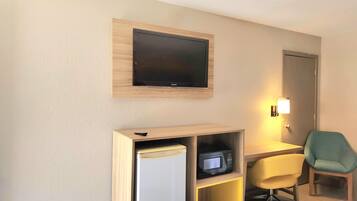 Une chambre d’hôtel équipée d’un téléviseur à écran plat fixé au mur, d’un minibar, d’un bureau avec une chaise et d’une table de chevet.