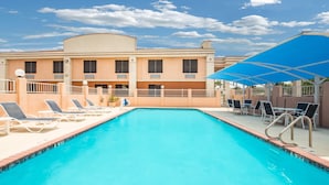 A swimming pool with lounge chairs and umbrellas, a building with a flat roof, and a clear sky. - Days Inn by Wyndham McAllen (McAllen)