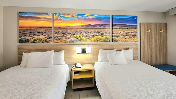 A hotel room with two beds, a large landscape painting, a wooden wardrobe, and a bedside table with a lamp. - Days Inn by Wyndham McAllen (McAllen)