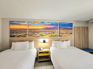Una camera d'albergo con due letti, un grande dipinto di paesaggio, un armadio in legno e un comodino con una lampada.