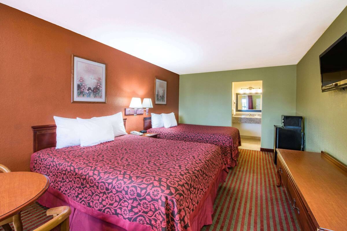 A hotel room with two beds, a desk, a chair, a TV, and a bathroom visible through an open door.