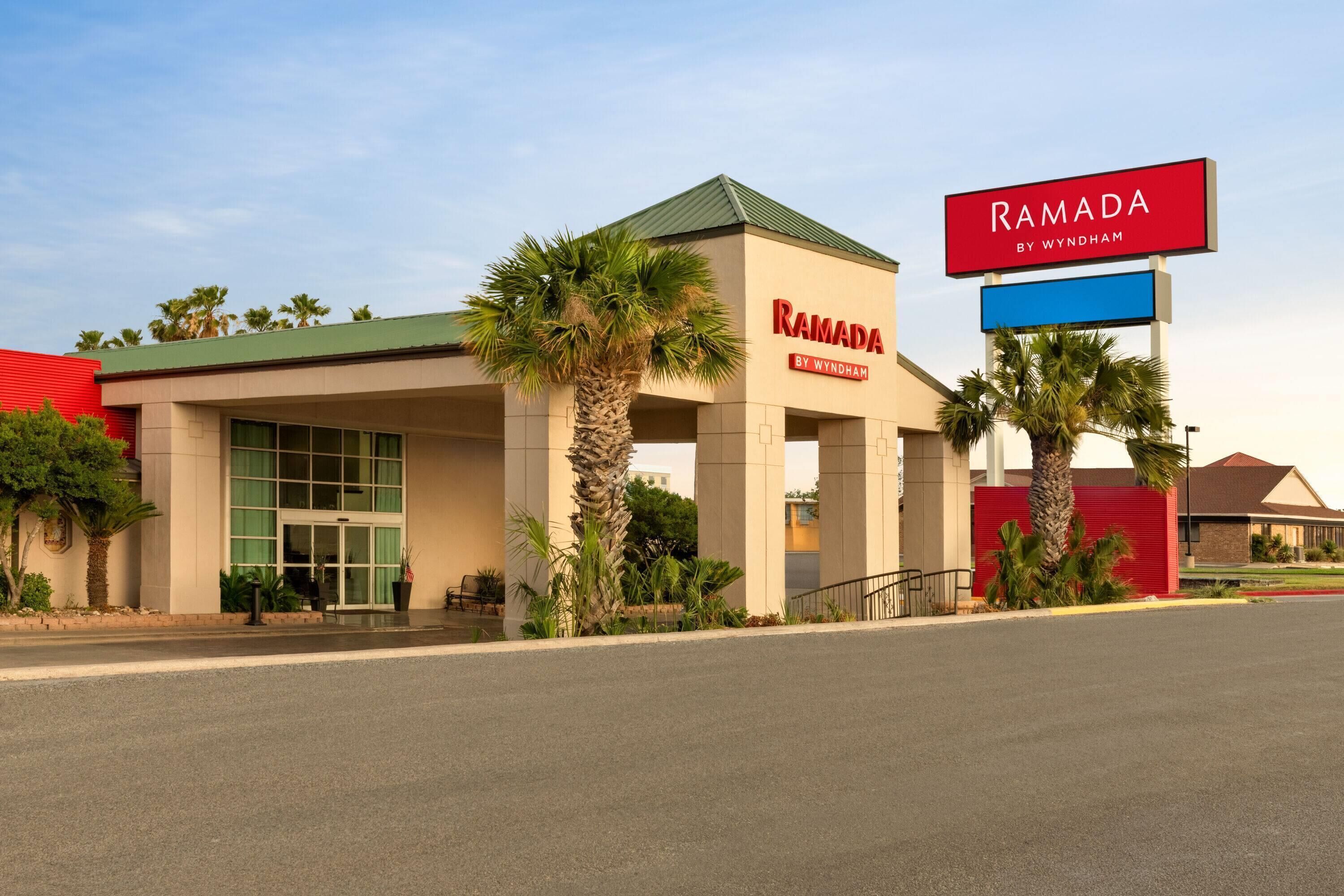 Et hotel kaldet Ramada by Wyndham med et moderne design, kendetegnet ved et markant rødt skilt, palmer og en velholdt facade.