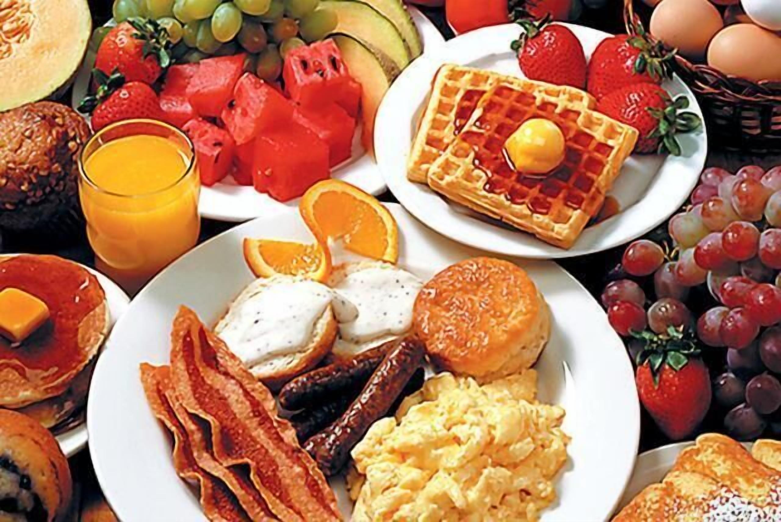 A breakfast spread with waffles, eggs, bacon, sausages, toast, and various fruits.