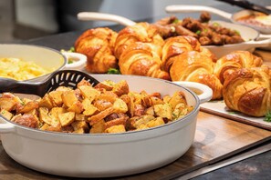A breakfast buffet with various dishes including croissants and roasted potatoes.