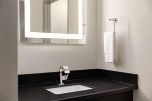 A modern bathroom with a black countertop, a chrome faucet, a rectangular mirror with a light, and a white towel hanging on a towel rack.