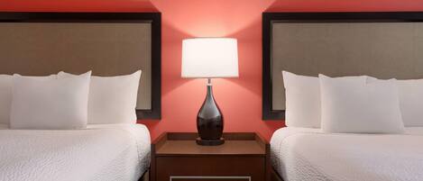 A hotel room with two beds, a nightstand with a lamp, and a red wall.